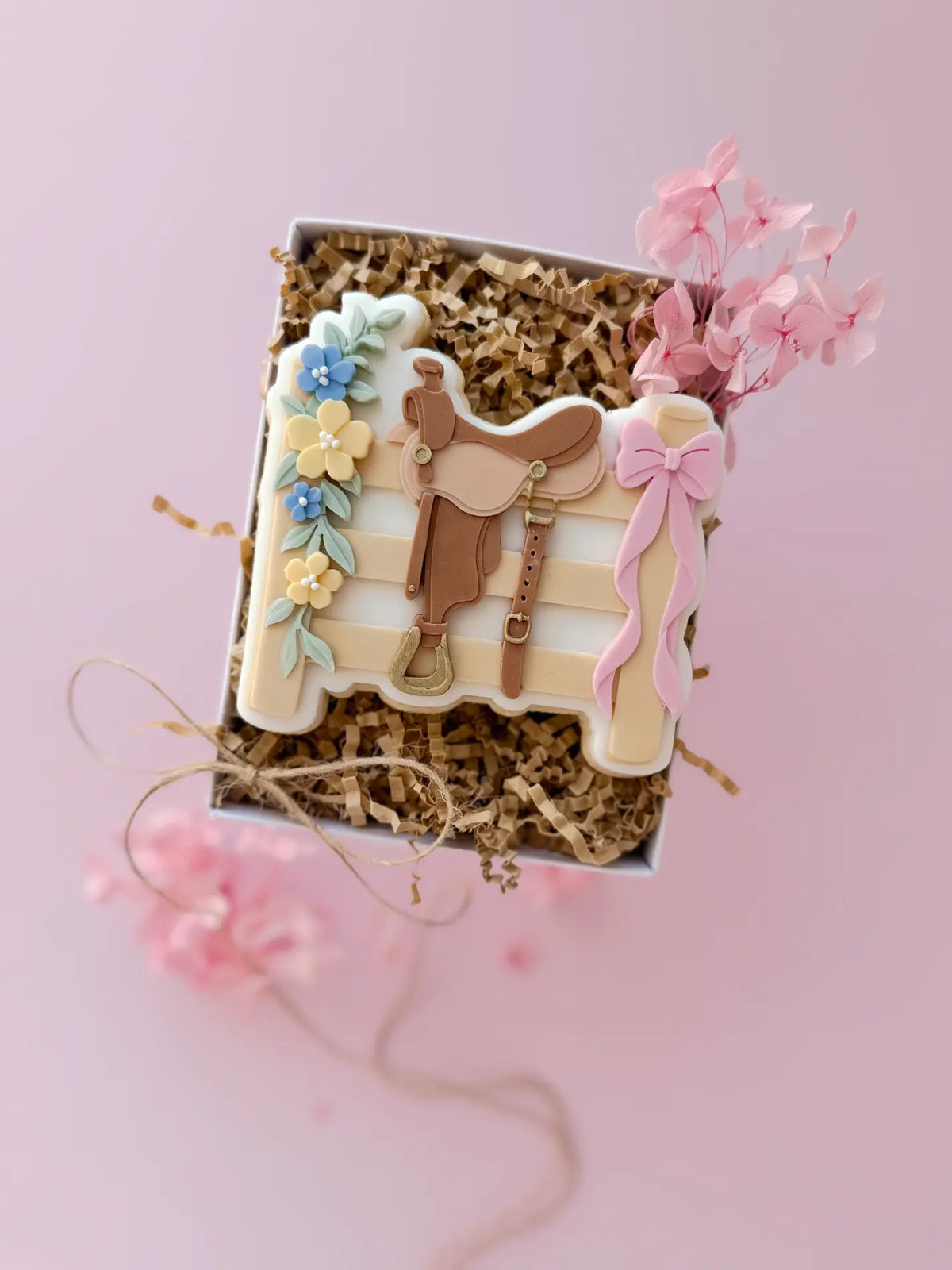 Dekorierter Keks mit Sattel, Steigbügel, Blüten und rosa Schleife in einer Geschenkbox – Anwendungsbeispiel / Decorated saddle cookie with stirrup, flowers and pink bow in a gift box – example of use