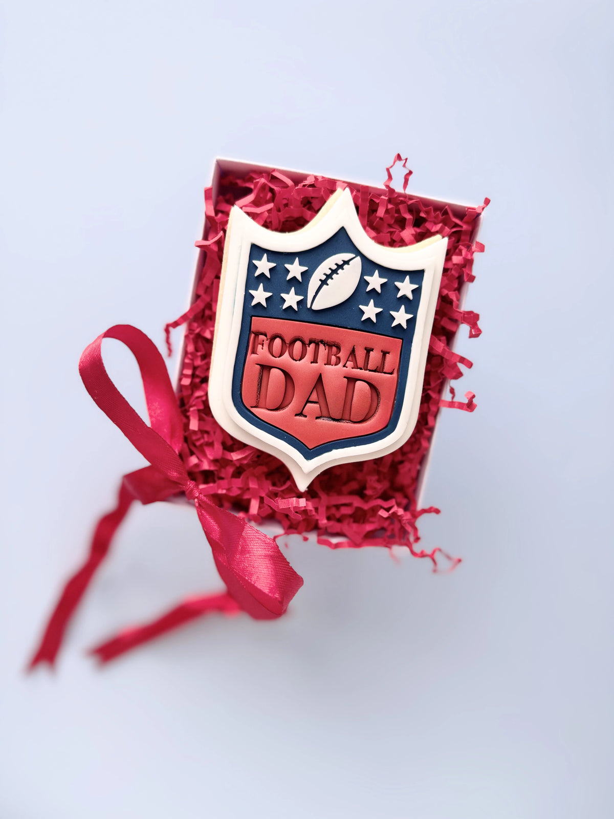 Football-Dad-Keks mit Schild, Sternen und Football in Rot, Weiss und Dunkelblau. Motivbeispiel von Danis Drip.