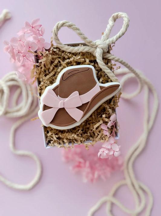 Verzierter Cowboyhut-Keks in Braun mit rosa Schleife in einer Geschenkbox.