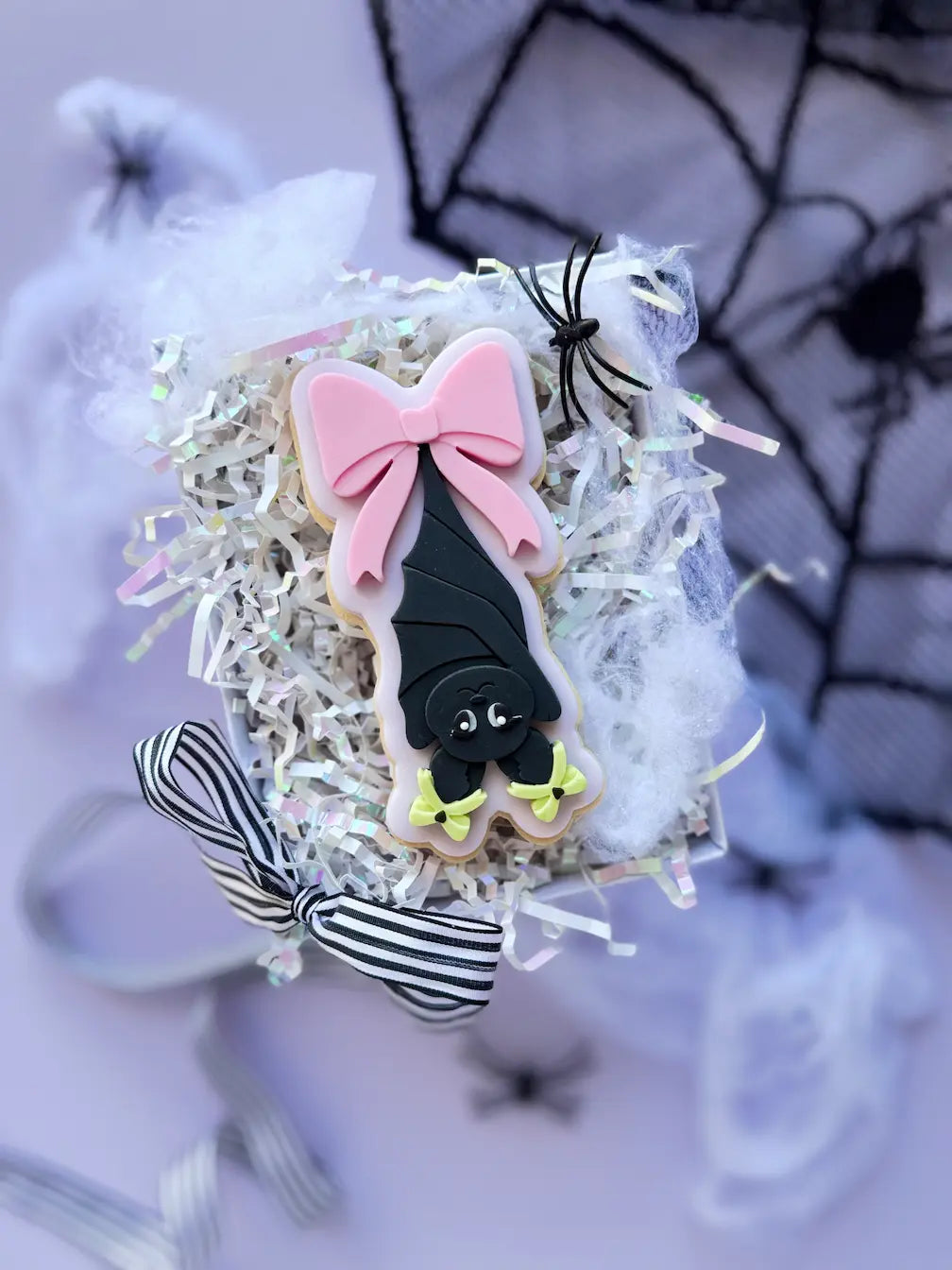 Dekorierter Halloween-Keks mit schwarzer kopfüber hängender Fledermaus und großer rosa Schleife.
