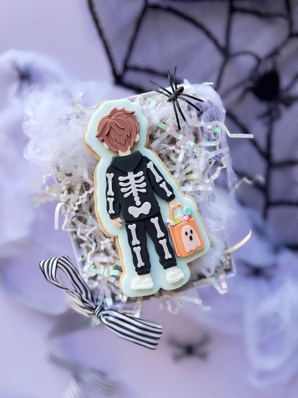 Dekorierter Halloween-Keks als Junge von hinten im schwarzen Skelettkostüm mit orangefarbener Süßigkeitentasche.