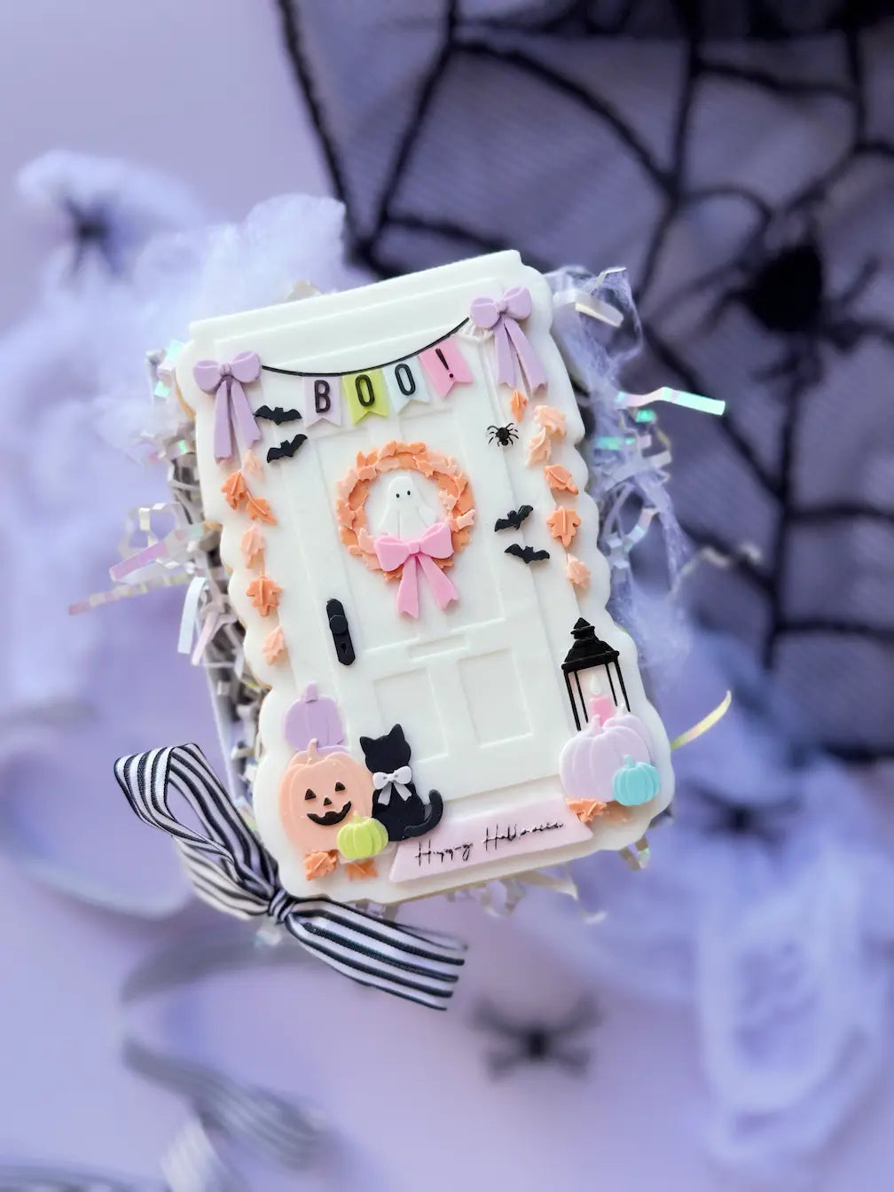 Dekorierter Keks als weiße Halloween-Tür mit BOO-Girlande, Geisterkranz, Kürbissen und schwarzer Katze.