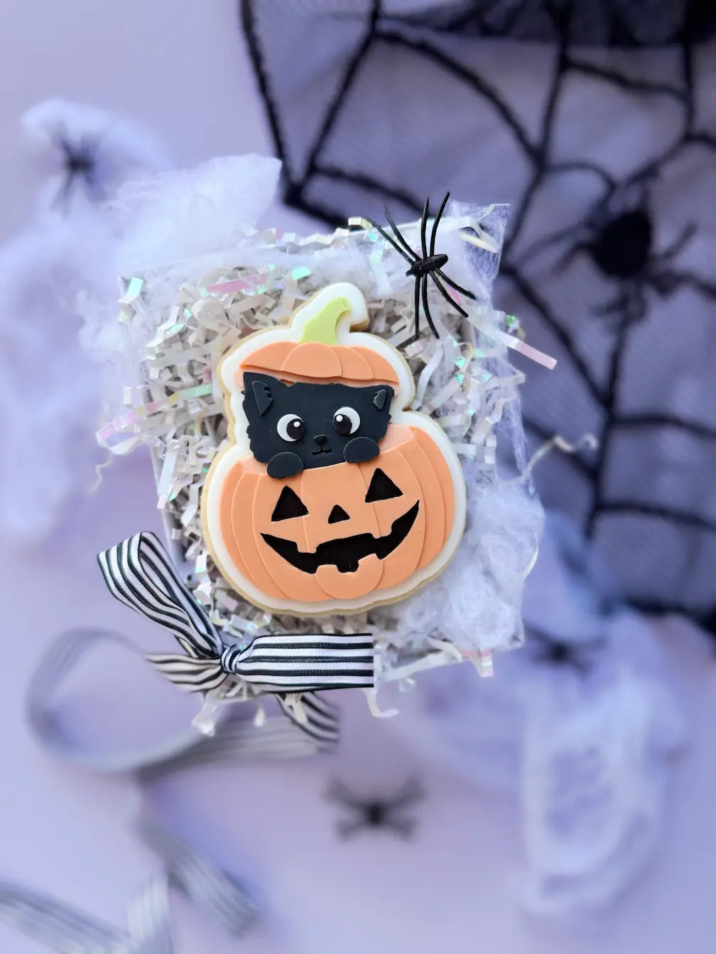 Dekorierter Halloween-Keks mit schwarzer Katze, die aus einem orangefarbenen Kürbis mit geschnitztem Gesicht schaut.