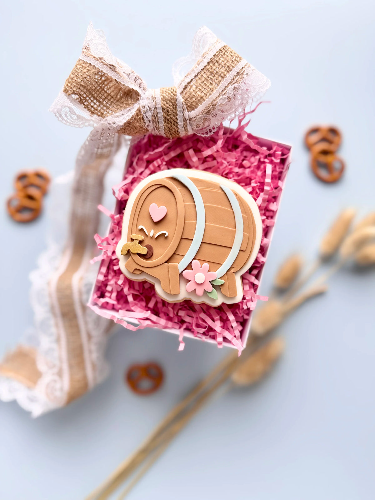 Verzierter Oktoberfest-Keks in Bierfassform mit rosa Herz und Blüten in einer Geschenkbox mit pinkem Füllpapier.