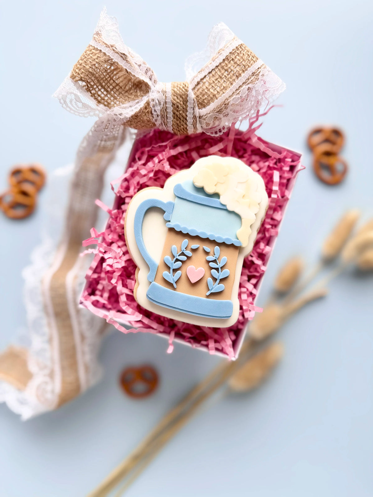 Verzierter Oktoberfest-Keks in Bierkrugform mit blauem Dekor, rosa Herz und weißem Schaum in einer Geschenkbox.