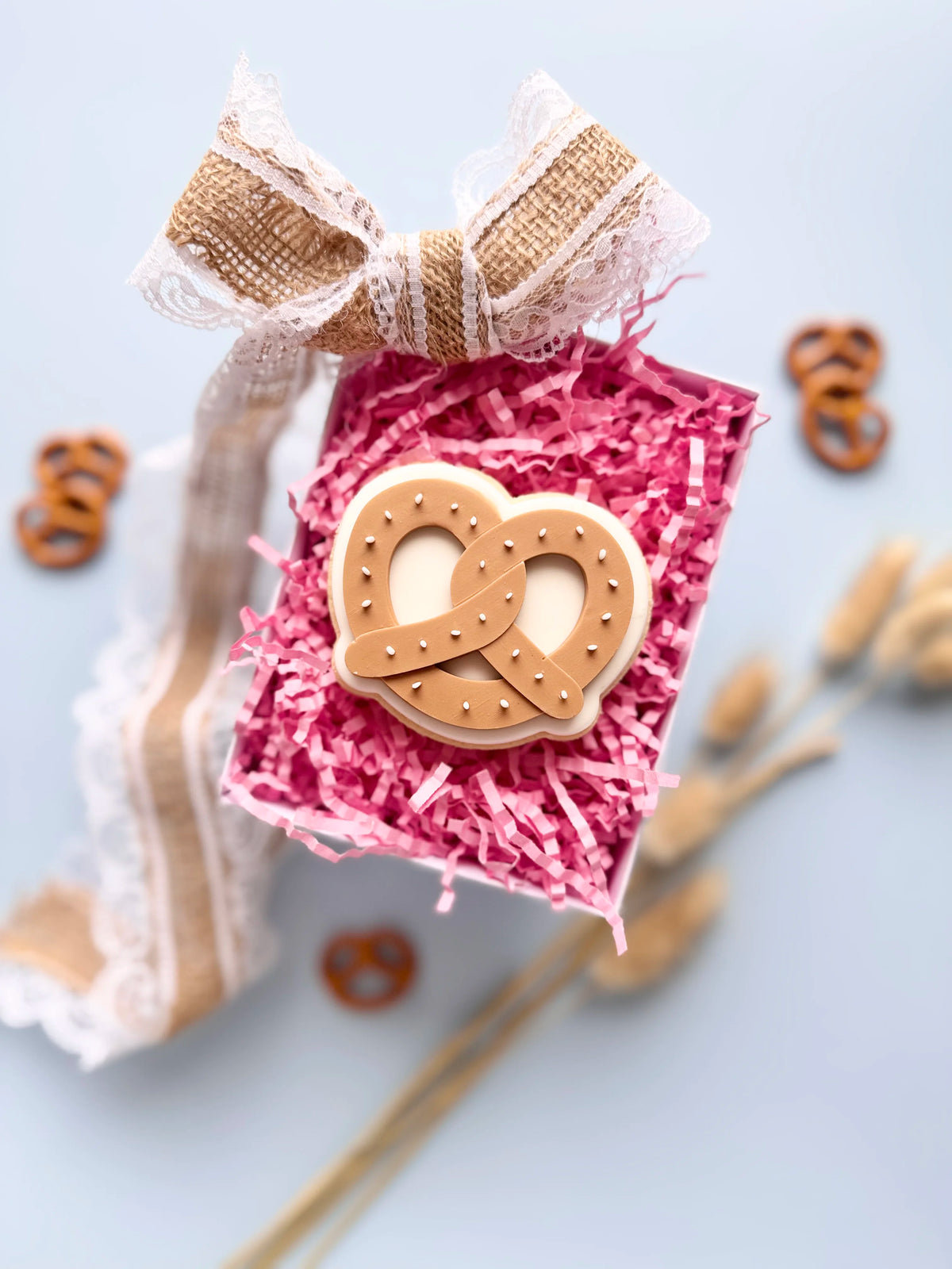 Verzierter Oktoberfest-Keks in Brezelform mit weißen Punkten in einer Geschenkbox mit pinkem Füllpapier und Juteschleife.