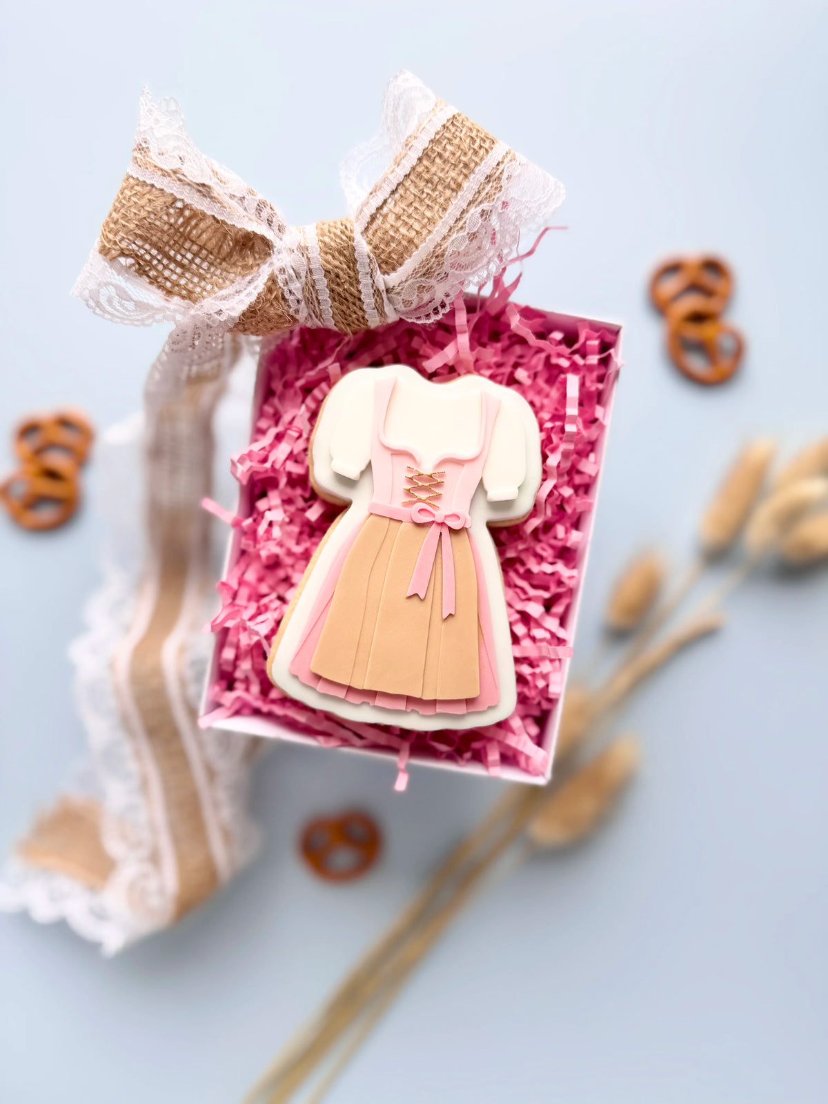 Verzierter Oktoberfest-Keks in Dirndlform mit rosa Schürze in einer Geschenkbox mit pinkem Füllpapier und Juteschleife.