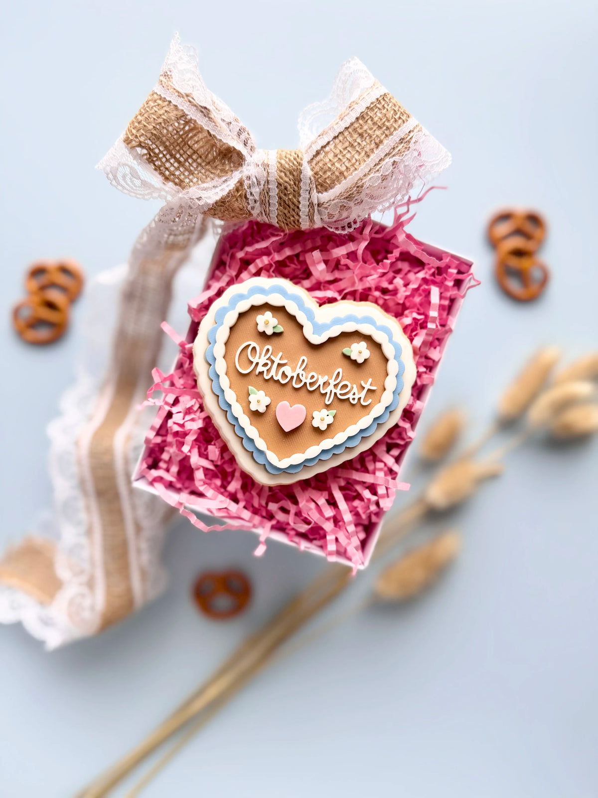 Herzförmiger Keks mit der Aufschrift „Oktoberfest“, blau-weißem Rand und kleinen Herzen in einer Geschenkbox.