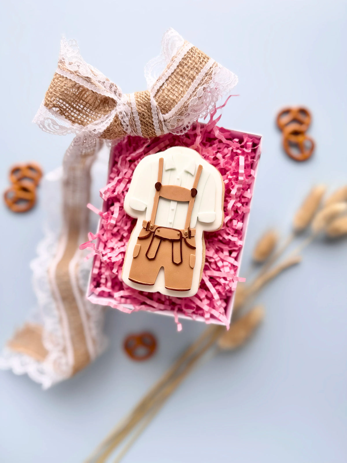 Verzierter Oktoberfest-Keks in Trachtenform mit brauner Lederhose, Hosenträgern und weißem Hemd in einer Geschenkbox.